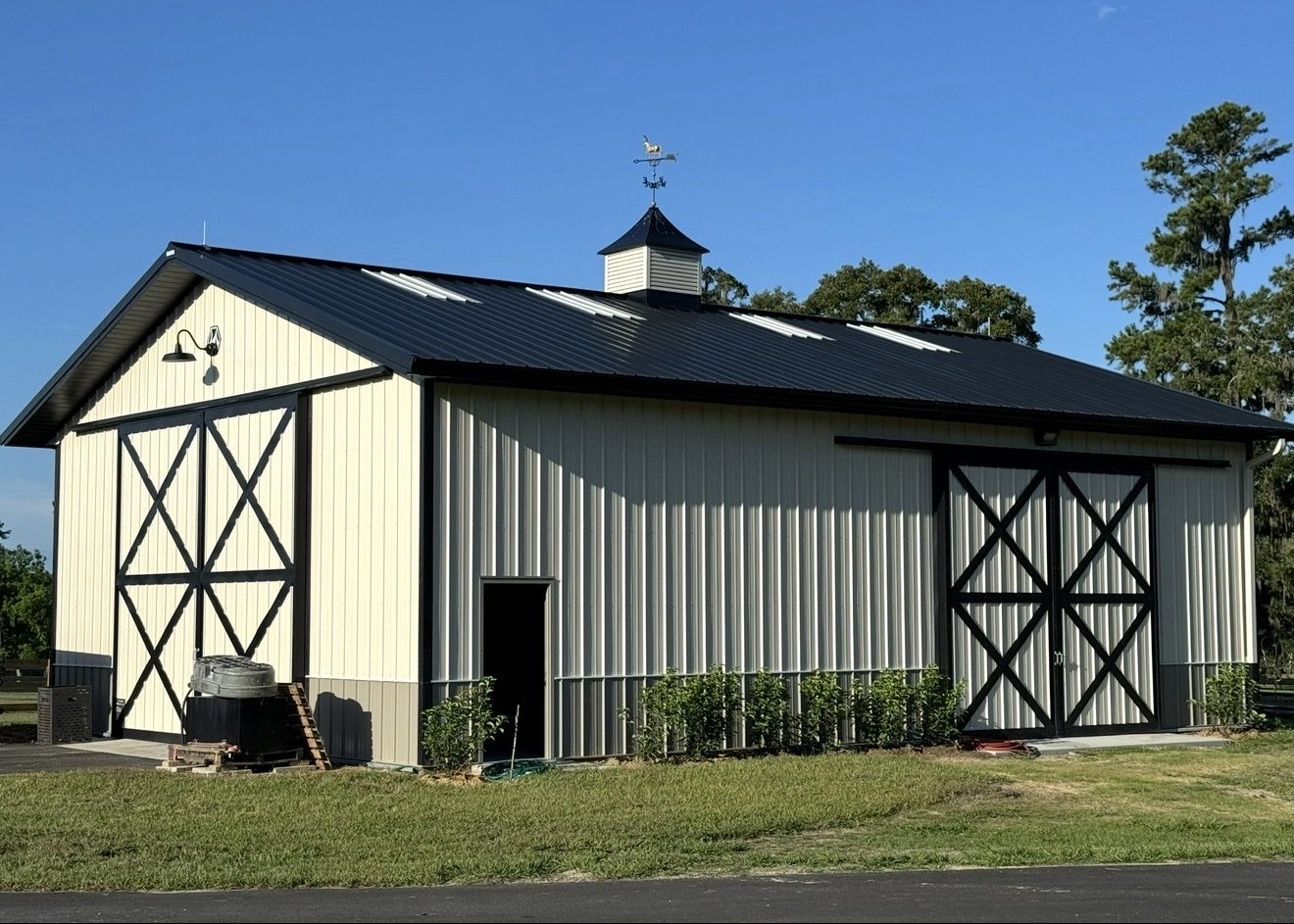 Cream-colored horse barn with black trim, cupola, and weathervane protected by lightning rods