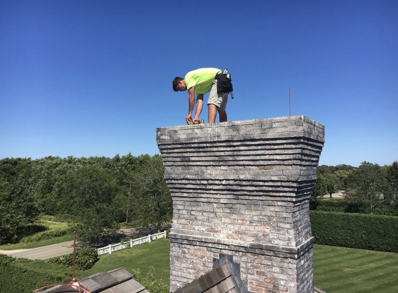 WB Lightning Rods crew member installing a copper lightning rod on top of a large stone chimney at a Hamptons estate